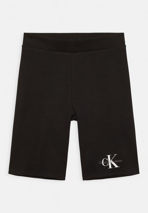Musta polven pituinen Calvin Klein Jeans -shortsi, jossa on joustava vyötärönauha ja valkoinen "CK"-logo vasemman jalan alaosassa.