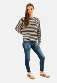 Zwart-wit gestreepte langemouwen shirt, blauwe skinny jeans en beige sneakers met donkere accenten. Soepele stof, casual ontwerp.