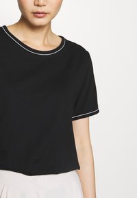 Czarny krótki rękaw, skrócony T-shirt z okrągłym dekoltem i białym akcentem na szwie przy kołnierzu i rękawach. Gładka tekstura.