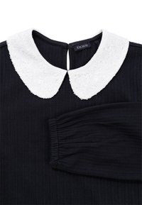 Czarny prążkowany top z długim rękawem z białą cekinową kołnierzem typu Peter Pan i zapięciem na guzik z tyłu w kształcie dziurki, metka marki "IKKS" wewnątrz kołnierza.