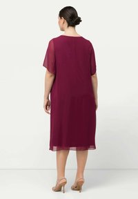 Robe en chiffon mauve avec des manches courtes, décolleté arrondi et coupe décontractée, arrivant au milieu du mollet. Portée avec des sandales à talons transparents. Texture lisse.