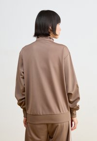 Brauner athletischer Pullover mit hohem Kragen, überschnittenen Schultern und geripptem Saum. Glatte Textur mit lockerer Passform, kombiniert mit passenden Hosen.