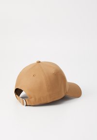 Baseball cap in a light brown fabric. Features a curved visor and adjustable strap at the back, smooth texture with stitching details.