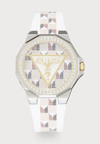 Montre avec bracelet en silicone blanc, boîtier en argent octogonal, cadran à motif, accents dorés et lunette en cristal. Présente le logo de la marque et un design triangulaire.