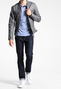 Grå læderjakke med teksturerede detaljer, blå t-shirt, mørke jeans og hvide sneakers. Jakken har en lynlåslomme og ståkrave.