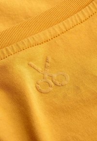 Geel katoenstof met een subtiele geborduurde schaaricoon, voorzien van een geribde tailleband en een gladde textuur.