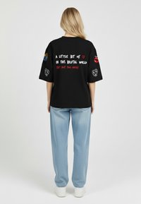 Black oversized t-shirt with colorful embroidered accents and text on the back. Paired with light blue denim pants and white shoes.