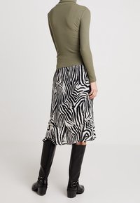 Olivgrüner, figurbetonter Rollkragenpullover, kombiniert mit einem schwarz-weißen Zebra-Musterrock mit Rüschensaum. Schwarze kniehohe Stiefel mit Hardware-Akzenten.