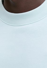 Hellblaues Sweatshirt mit einem gerippten Kragen, glatter Textur und nahtlosem Design, das Stoffkonsistenz und zurückhaltenden Stil zeigt.