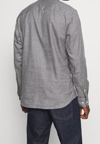 Szara flanelowa koszula z kołnierzykiem na guziki, długimi rękawami i białymi guzikami. Charakteryzuje się subtelną fakturą i zaokrąglonym dołem.