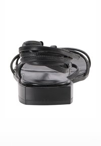 Sandal din piele neagră cu mai multe curele subțiri și toc mic, prezentată din spate pe un fundal alb.