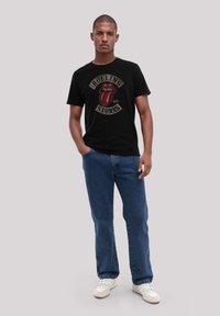 Zwart katoenen T-shirt met het logo van de Rolling Stones en een rode tong graphic. Gecombineerd met blauwe spijkerbroek en witte sneakers.