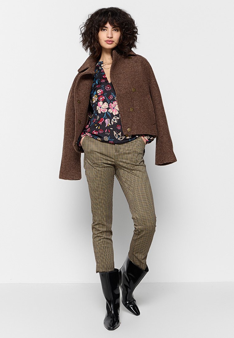 Cappotto corto in misto lana marrone, blouse a stampa floreale, pantaloni a quadri testurizzati in tonalità terrose e stivali neri lucidi al ginocchio.