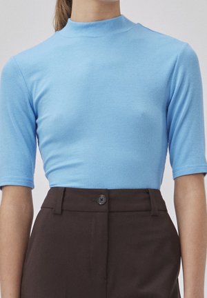 Top azzurro chiaro a costine con maniche corte e scollatura alta, abbinato a pantaloni marrone scuro con un dettaglio a bottone singolo.