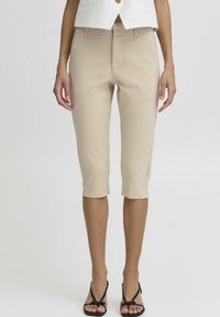 Pantalons beige raccourcis avec une texture lisse, dotés d'une poche avant et d'un ourlet à revers, associés à un haut sans manches blanc.