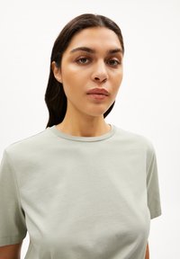 Helles grünes T-Shirt aus weichem, glattem Baumwollmaterial mit Rundhalsausschnitt und kurzen Ärmeln, das eine taillierte Silhouette und ein minimales Design aufweist.