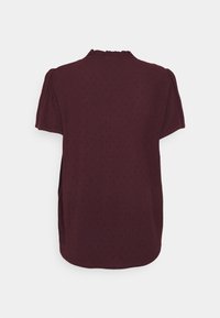 Krótki rękaw ciemno-bordowej bluzki z delikatną kropeczkową teksturą, lekko falbaniastym kołnierzykiem i marszczonymi detalami na ramionach na białym tle.