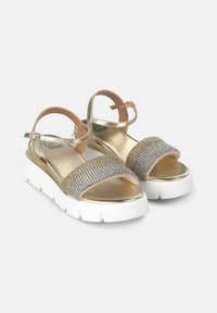 Goldene Sandalen mit einem breiten, mit Schmuck besetzten Riemen und verstellbarem Knöchelverschluss, ausgestattet mit einer weißen Plateau-Sohle. Glatte Textur mit funkelnden Akzenten.