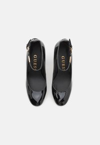 Scarpe in vernice nera con un design elegante, punte quadrate e una fascia con una fibbia dorata. L'interno presenta una fodera nera liscia.