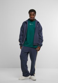 Trening bleumarin cu un sacou cu fermoar și pantaloni cu dungi pe lateral. Material din bumbac, croială lejeră, asortat cu adidași albi.