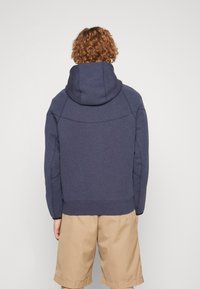 Mörkblå hoodie med en stor huva, raglanärmar och ribbad nederkant. Mjukt, texturerat tyg; enkel design utan mönster eller detaljer.