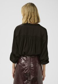 Zwarte, vloeiende blouse met een ronde hals en losse mouwen, gecombineerd met een aansluitende, glanzende bordeauxrode rok met een centrale rits.