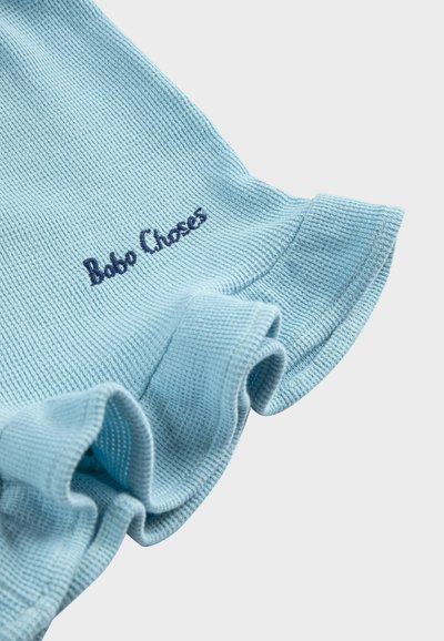 Tissu bleu clair texturé avec bordure froncée et "Bobo Choses" brodé en fil bleu foncé.