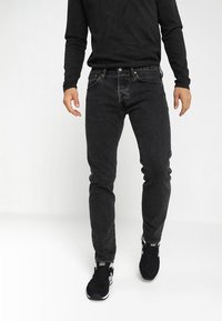 Svarta skinny jeans i denim med en texturerad yta, kombinerat med en svart långärmad tröja och svarta sportskor.