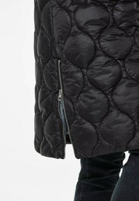 Zwarte gewatteerde pufferjack met een kenmerkend cirkelpatroon, zijritssluiting en een gladde textuur, geschikt voor koud weer.