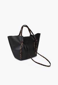 Black leather tote bag with a textured finish, featuring leopard print handles and a spacious design with ties for closure.