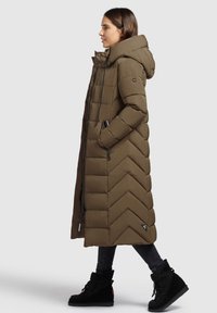 Garšs, brūns pūkains mētelis ar zigzag rakstu, liels kapucis, ar rāvējslēdzēju aizdare priekšpusē un sānu kabatas. Valkāts virs melnām biksēm un melniem zābakiem.