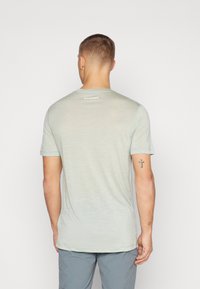 Lichtgroene T-shirt met korte mouwen, gemaakt van textuurstof, met een ronde hals en een subtiel logo op de achterkant. Minimalistisch ontwerp.
