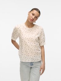 Floral-patterned short-sleeve blouse in light beige with round neckline and soft fabric; worn with light-wash denim pants.