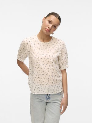 Floral-patterned short-sleeve blouse in light beige with round neckline and soft fabric; worn with light-wash denim pants.