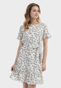 Valkoinen mekko mustalla kukkakuviolla, lyhyet röyhelöpuolet, istuva vyötärö yhteensopivalla soljella ja liehuva helma röyhelöillä.