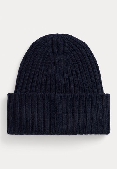 Beanie tricotat de culoare bleumarin, cu o textură striată și margine pliată. Dispune de linii verticale discrete și un design cu vârf rotunjit.