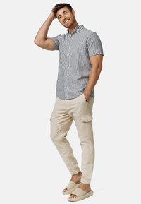 Camisa de manga corta con cuello y rayas verticales azul y blancas, combinada con pantalones cargo beige claro y sandalias beige de tipo slip-on.
