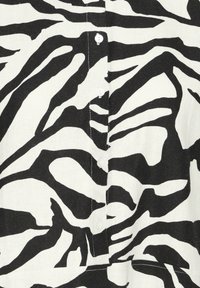 Gros plan sur un tissu rayé zébré noir et blanc avec quatre boutons blancs en rangée verticale et des coutures visibles le long de la patte de boutonnage.