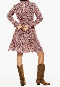 Abito floreale rosa con colletto e maniche lunghe, presenta una gonna a strati ed è abbinato a stivali da cowboy marroni.