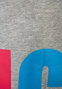 Grå bomullstyg med struktur. Har en grafikdesign i blått och rosa, med en präglad logotyp som liknar en svamp.