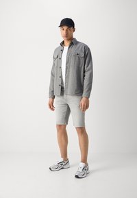 Gray button-up shirt with two front pockets, white T-shirt, light gray shorts, and gray New Balance sneakers, complemented by a black cap.
