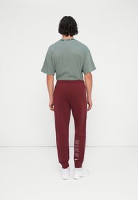 Zelena majica s relaxed fit krojem, uparena s burgundijim joggericama sa bijelim bočnim stranama i "NIKE" logotipom. Bijele tenisice upotpunjuju odjevnu kombinaciju.