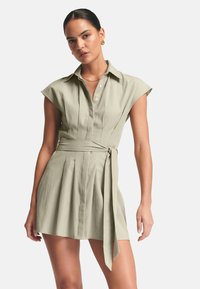 Hellgrünes Hemdkleid mit kurzen Kappenärmeln, durchgehender Knopfleiste, plissiertem Rock und einem gebundenen Taillendetail. Glatter, gewebter Stoff.