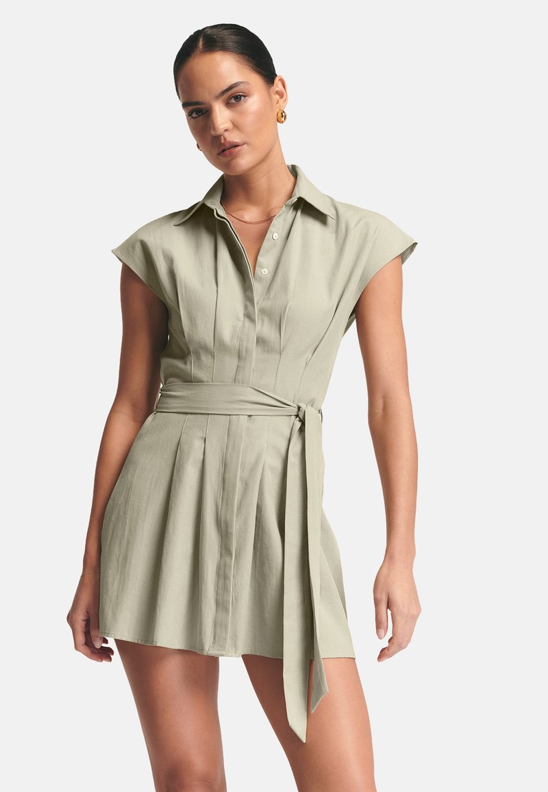 Hellgrünes Hemdkleid mit kurzen Kappenärmeln, durchgehender Knopfleiste, plissiertem Rock und einem gebundenen Taillendetail. Glatter, gewebter Stoff.