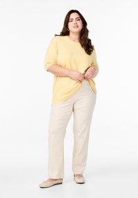 Gul strikket sweater med korte ærmer, parret med beige lige bukser og lyse beige flade sko. Blød tekstur, afslappet pasform.