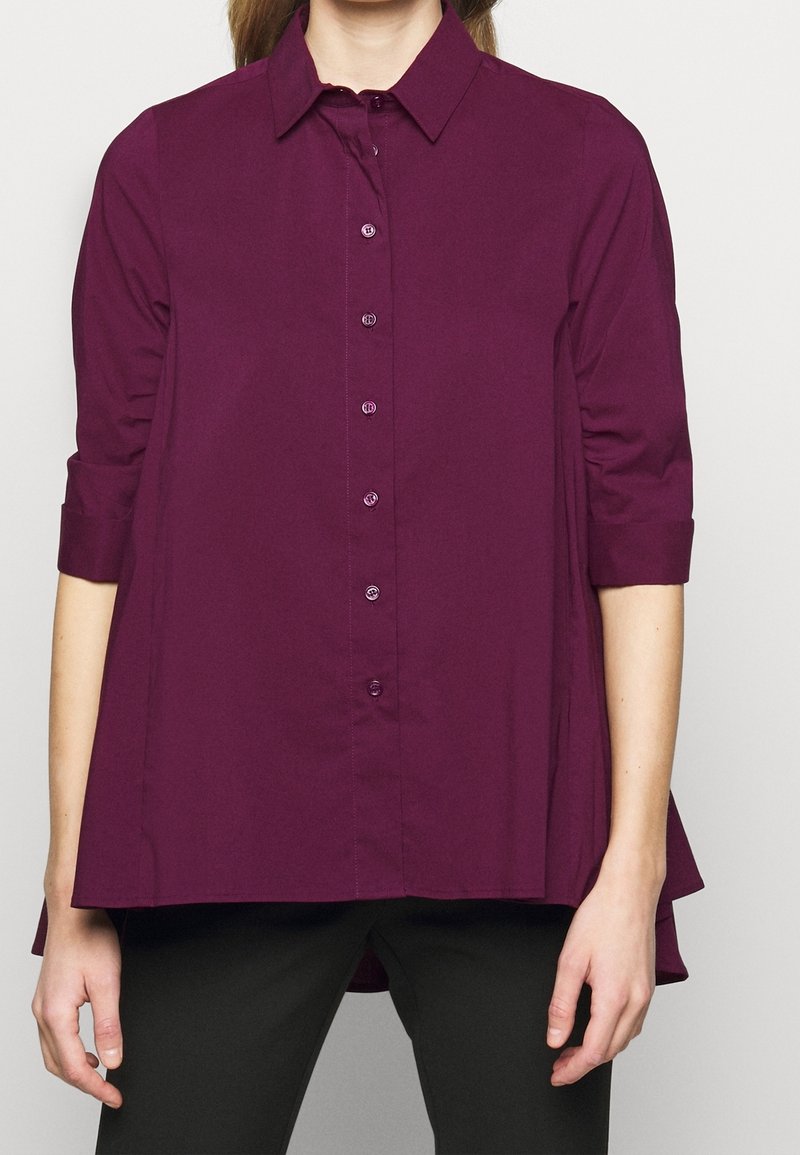 Lila skjorta med knappar, krage, och trekvartsärmar. Har en utsvängd design och subtil lyster. Lätt textur, halvslimmad.