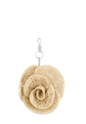 Beżowy pleciony brelok w kształcie kwiatu z warstwowymi płatkami oraz srebrnym metalowym zatrzaskiem i pierścieniem do przyczepienia.