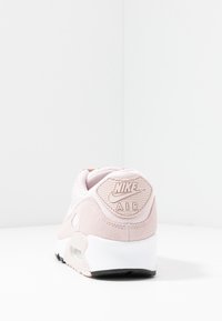 Baskets Nike Air rose clair avec une tige en daim, un collier rembourré, une semelle en caoutchouc et un talon texturé avec un logo.