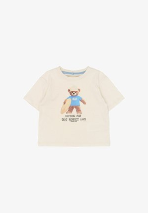 Lysebeige T-shirt med korte ærmer, med et motiv af en bjørn iført blå skjorte, der holder et surfbræt, med teksten: "Venter på den perfekte bølge".