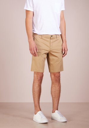 Beżowe bawełniane szorty z płaskim przodem, szlufkami na pasek i pojedynczym zapięciem na guzik. W połączeniu z białą koszulką z krótkim rękawem i białymi treningami.